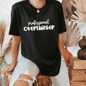 May include: Black t-shirt with white text that reads "professional overthinker".