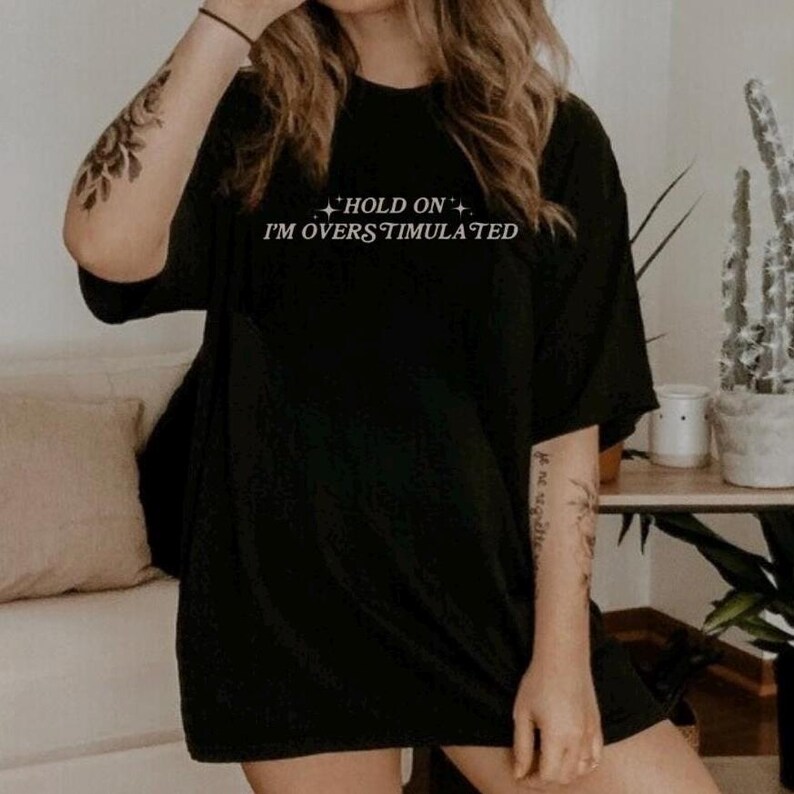 Może przedstawiać: Czarny, oversize'owy T-shirt z napisem "Hold On I'm Overstimulated" w kolorze białym.