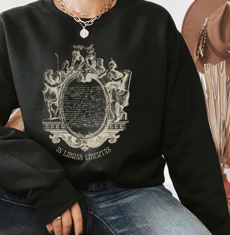 May include: Black sweatshirt with a vintage-style graphic print of a crest featuring a quote in a circle, two figures, and the text "In Libras Libertas".