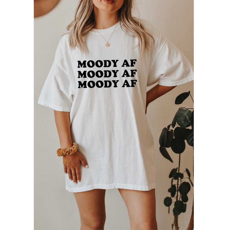 May include: White oversized t-shirt with black text that reads "MOODY AF" repeated three times.
