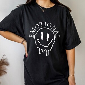 May include: Black t-shirt with a white dripping smiley face and the word "EMOTIONAL" written around it.