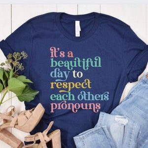 May include: A navy blue t-shirt with the text "It's a beautiful day to respect each others pronouns" in rainbow colors.