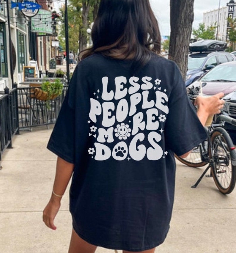 May include: Black t-shirt with a white graphic that says "Less People More Dogs" in a retro font. The graphic also includes a flower with a smiley face and a paw print.