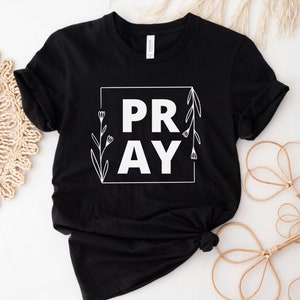 May include: Black t-shirt with a white graphic that says "PRAY" in a square frame with floral accents.