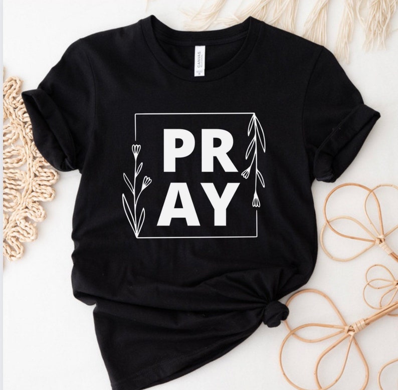 May include: Black t-shirt with a white graphic that says "PRAY" in a square frame with floral accents.
