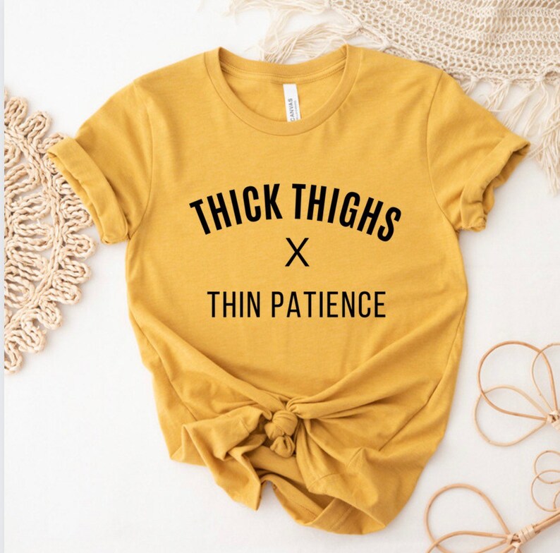May include: A mustard yellow t-shirt with the text "THICK THIGHS x THIN PATIENCE" printed in black.