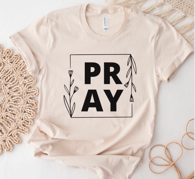 May include: A beige t-shirt with a black graphic that says "PRAY" with floral accents.