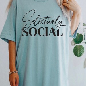 May include: A light blue t-shirt with the text "Selectively Social" printed in black.