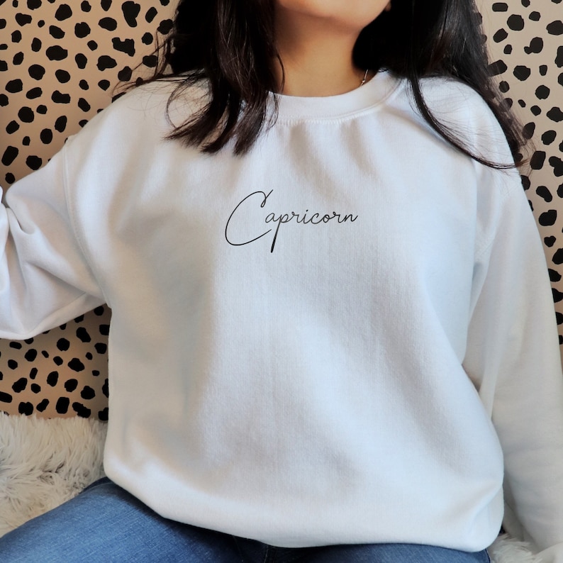 May include: White sweatshirt with the word "Capricorn" written in cursive on the front.