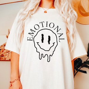 May include: White t-shirt with a black dripping smiley face and the word "EMOTIONAL" written around it.