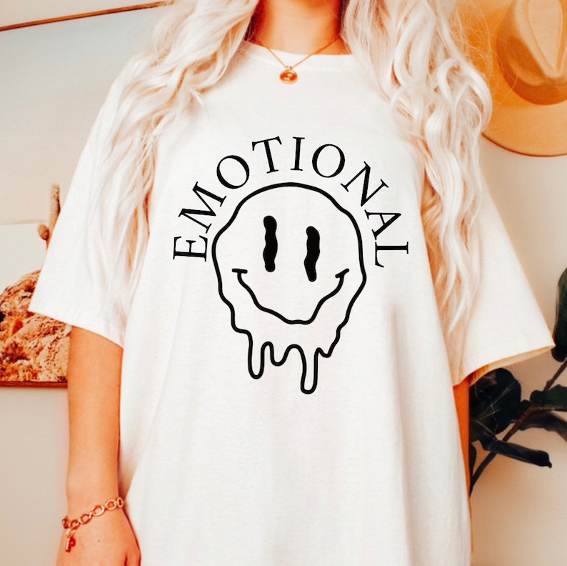 May include: White t-shirt with a black dripping smiley face and the word "EMOTIONAL" written around it.