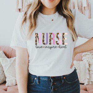May include: White t-shirt with the word "NURSE" in pink, purple, and brown leopard print letters. The text "love inspire heal" is below the word "NURSE" in a smaller font.