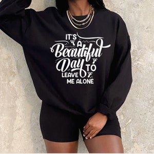 May include: Black sweatshirt and shorts set. The sweatshirt features the white text, "It's a Beautiful Day to Leave Me Alone." The outfit is paired with a gold necklace. The clothing set is a casual, comfortable style.