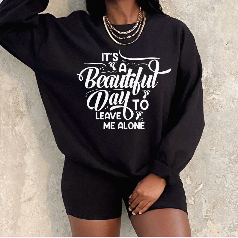 May include: Black sweatshirt and shorts set. The sweatshirt features the white text, "It's a Beautiful Day to Leave Me Alone." The outfit is paired with a gold necklace. The clothing set is a casual, comfortable style.
