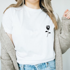 K&ouml;nnte beinhalten: Ein wei&szlig;es T-Shirt mit einer schwarzen Silhouette einer Rose auf der linken Brustseite.