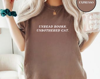 Może przedstawiać: Brązowa koszulka z nadrukiem "Unread Books. Unbothered Cat." w kolorze białym.