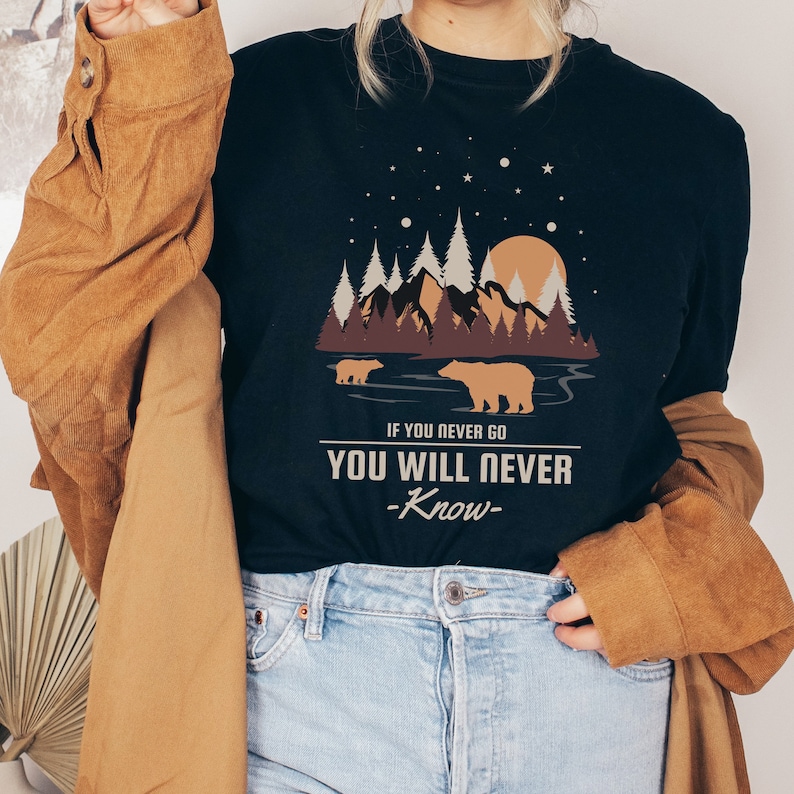 May include: A black t-shirt with a graphic of a mountain range, two bears, and a moon with stars. The text on the shirt reads "If you never go, you will never know."