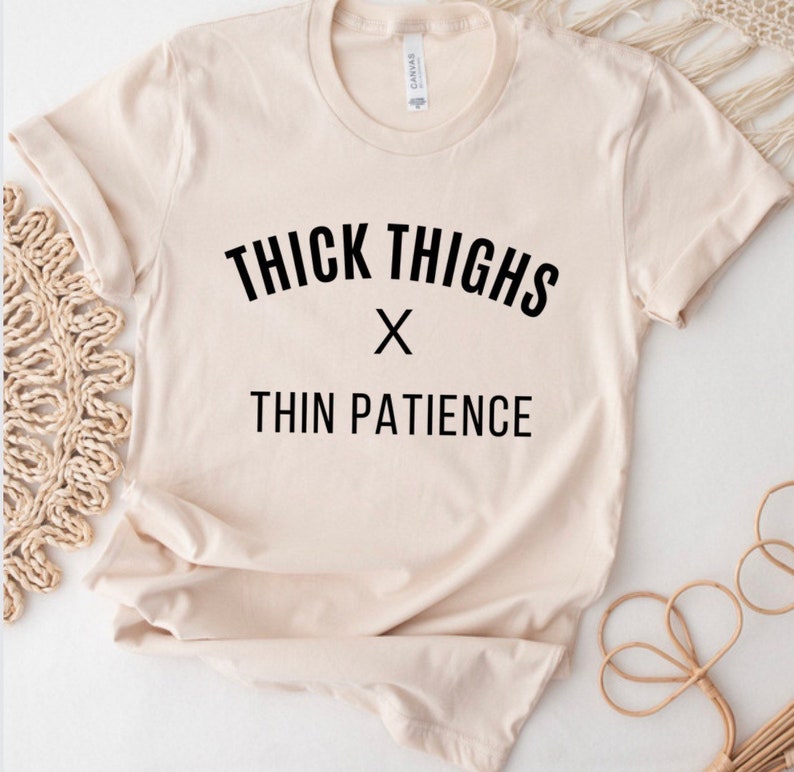 May include: A beige t-shirt with black text that reads "THICK THIGHS x THIN PATIENCE".
