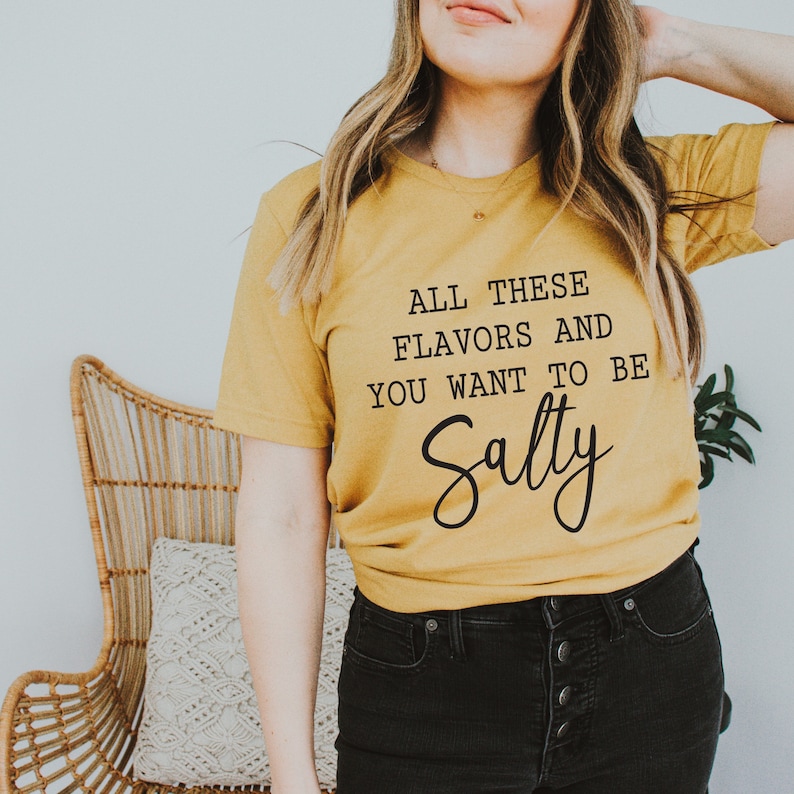 May include: A mustard yellow t-shirt with the text "All these flavors and you want to be Salty" in black lettering.