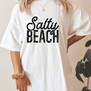 May include: White t-shirt with black text that reads "Salty Beach" in a distressed font.