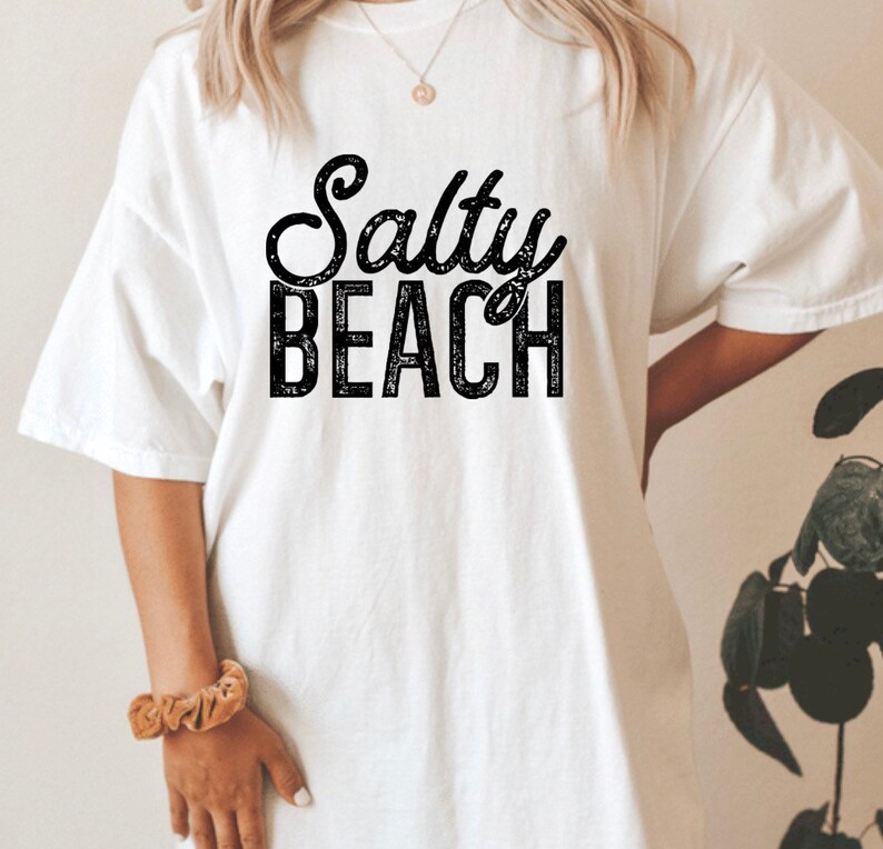 May include: White t-shirt with black text that reads "Salty Beach" in a distressed font.