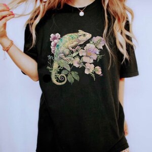 May include: Black t-shirt featuring a green chameleon and pink flowers printed on the front.