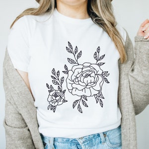 K&ouml;nnte beinhalten: Ein wei&szlig;es T-Shirt mit einer schwarzen Linienzeichnung von zwei Blumen und Bl&auml;ttern.