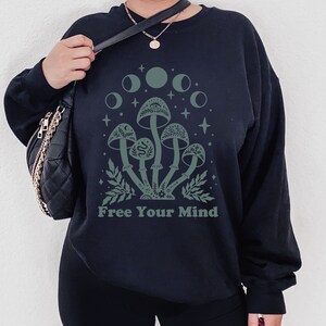 以下が含まれることがあります： 「Free Your Mind」というテキストと、緑色のキノコのグラフィックが描かれた黒いスウェットシャツ。