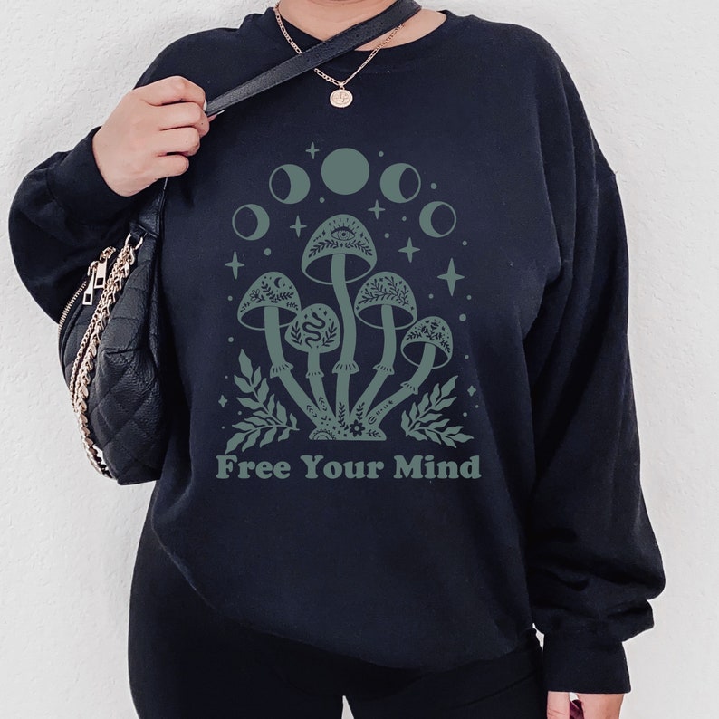 以下が含まれることがあります： 「Free Your Mind」というテキストと、緑色のキノコのグラフィックが描かれた黒いスウェットシャツ。