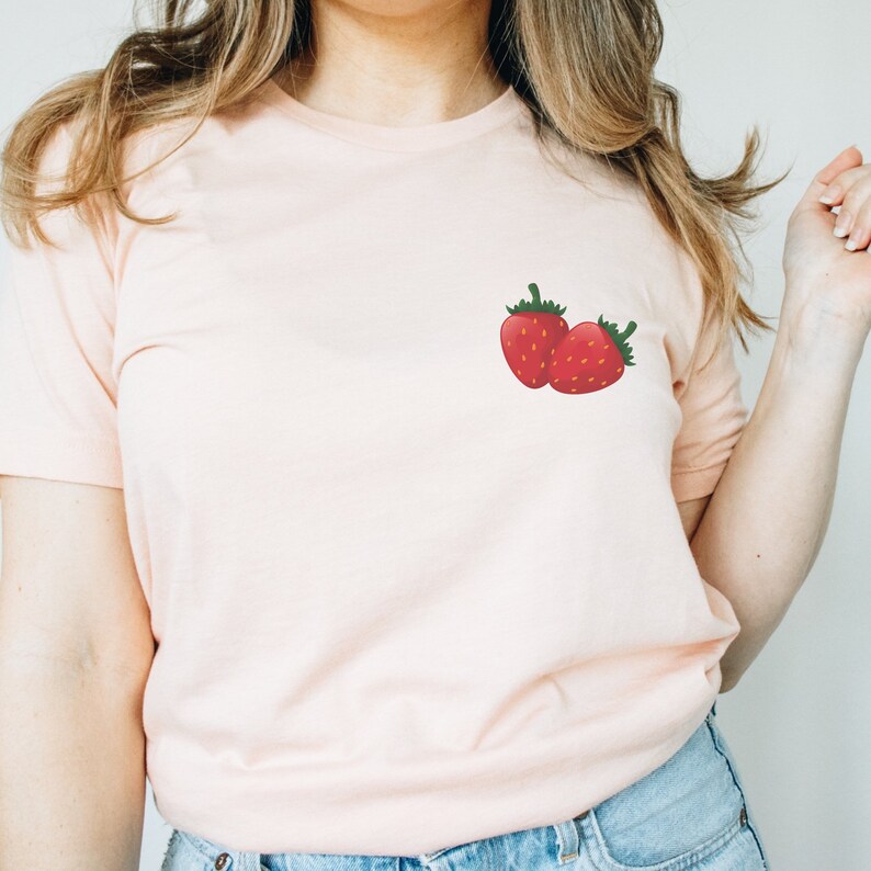 Peut inclure: Un t-shirt rose p&acirc;le avec un petit motif de deux fraises rouges sur le c&ocirc;t&eacute; gauche de la poitrine.