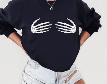 May include: A black sweatshirt with a white skeleton hand graphic on the front. The hands are positioned as if they are covering the chest. The sweatshirt is being worn by a person.
