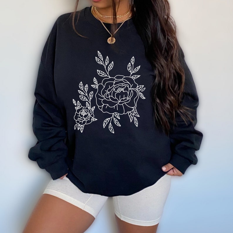 K&ouml;nnte beinhalten: Schwarzer Pullover mit einem wei&szlig;en Umriss eines Blumendesigns mit zwei Rosen und Bl&auml;ttern.