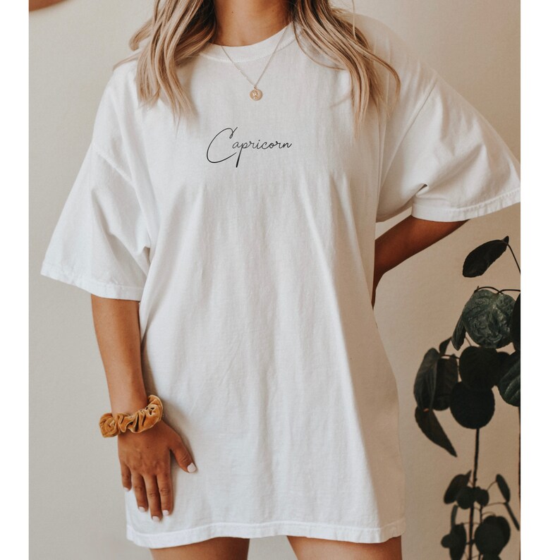 May include: White oversized t-shirt with a black cursive inscription "Capricorn" on the front.