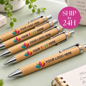 May include: Five bamboo ballpoint pens with silver-toned metal clips and tips. Each pen features a printed multi-colored lotus flower graphic and the black text "YOUR LOGO HERE" or "YOUR TEXT HERE" displayed along the wooden barrel surface.