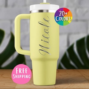 May include: A light yellow insulated tumbler with a handle, white lid, and straw. The name "Nicole" is written in silver script. A circular graphic indicates "20+ COLORS".