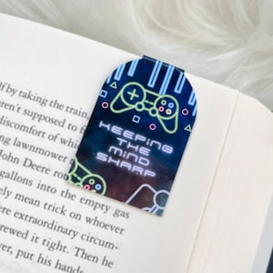 May include: A black and blue magnetic bookmark with a neon green and blue video game controller graphic. The bookmark has the text "Keeping the Mind Sharp" on it.