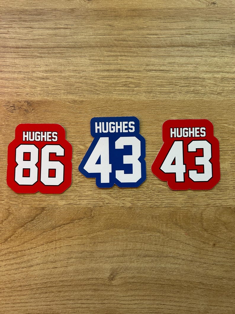 Puede incluir: Tres pegatinas rectangulares con el nombre "HUGHES" encima de n&uacute;meros grandes. Una pegatina es roja con texto blanco y el n&uacute;mero "86". Las otras dos pegatinas son azules y rojas con el n&uacute;mero "43".