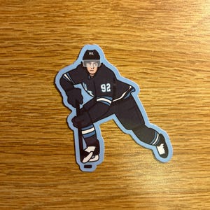 May include: A sticker featuring a stylized illustration of a hockey player in a dark blue uniform with the number 92. The player is in a skating pose, holding a hockey stick, with a light blue outline.