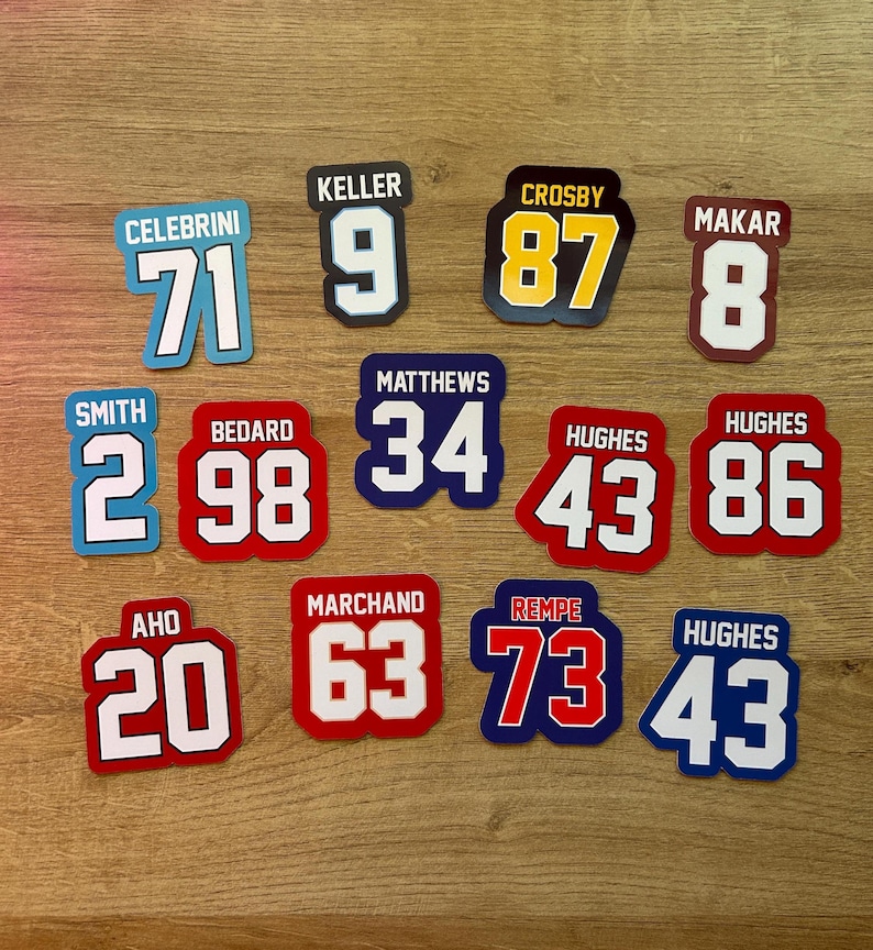 Puede incluir: Una colecci&oacute;n de pegatinas con n&uacute;meros estilo camiseta de hockey. Cada pegatina presenta el nombre y el n&uacute;mero de un jugador, con varios esquemas de color, incluyendo azul, rojo y amarillo. Los n&uacute;meros van del 2 al 98.