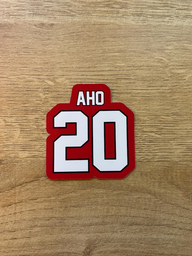 Puede incluir: Una pegatina roja y blanca con el texto "AHO" encima del n&uacute;mero "20". Los n&uacute;meros y letras blancos tienen un contorno negro sobre un fondo rojo. La pegatina es rectangular con esquinas redondeadas.