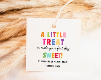 Peut inclure: Une étiquette cadeau carrée blanche avec le texte "A LITTLE TREAT to make your first day SWEET!" en lettres colorées. L'étiquette comprend également les phrases "It's going to be a great year!" et "FROM MISS JANICE".