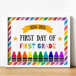 May include: A framed print with the text "2024-2025 FIRST DAY OF FIRST GRADE" in black and rainbow colors. The design includes colorful crayons at the bottom and a striped border in various colors. Two gold stars flank the words.