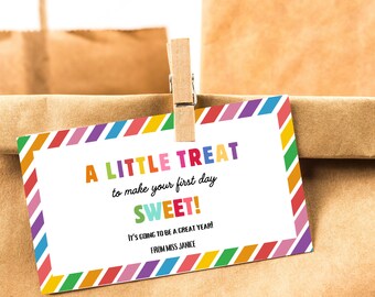 Peut inclure: Une étiquette cadeau rectangulaire avec une bordure rayée colorée et le texte "A LITTLE TREAT to make your first day SWEET!" est attachée à un sac en papier brun. L'étiquette indique également "IT'S GOING TO BE A GREAT YEAR! FROM MISS JANICE."