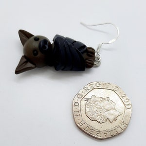 May include: A pair of brown and black bat earrings with silver hooks. The bat is wrapped in a dark blue fabric.