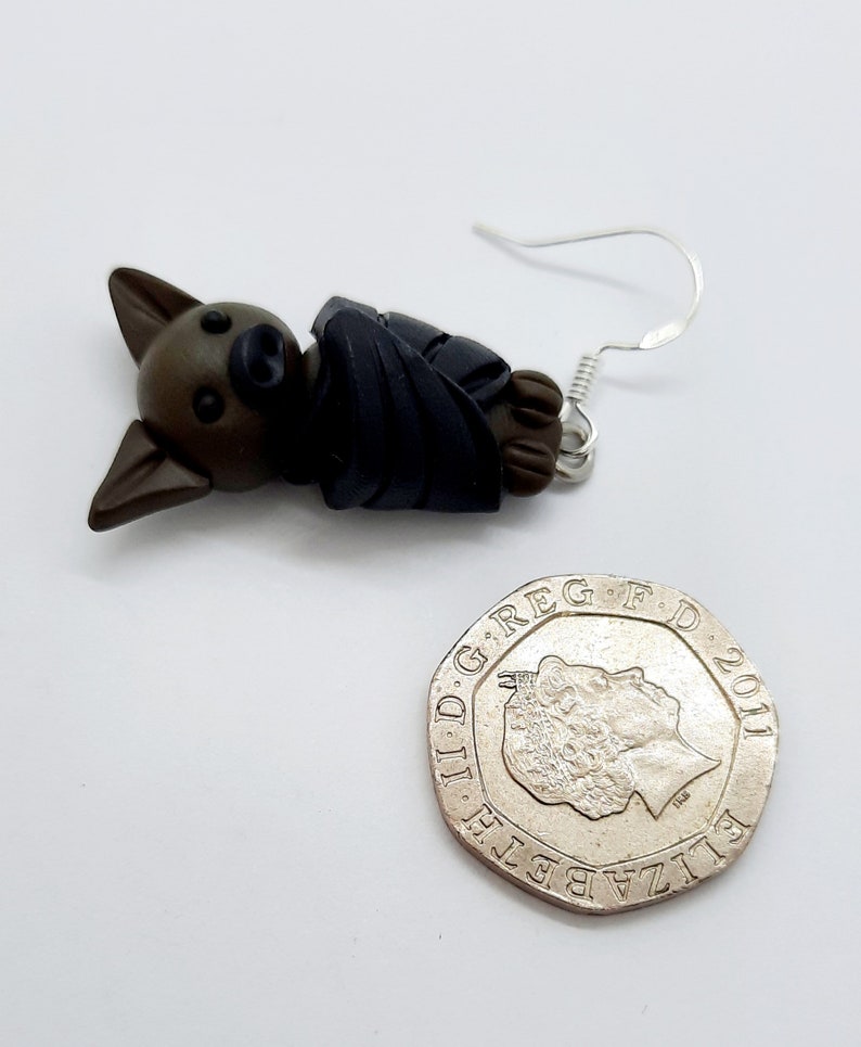 May include: A pair of brown and black bat earrings with silver hooks. The bat is wrapped in a dark blue fabric.