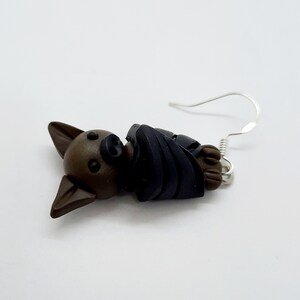 May include: A pair of brown and black bat earrings with silver hooks. The bat is curled up in a sleeping position.