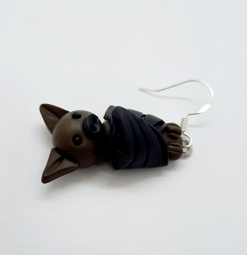 May include: A pair of brown and black bat earrings with silver hooks. The bat is curled up in a sleeping position.