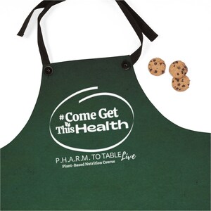 May include: Green apron with black straps and white text that reads "#Come Get This Health P.H.A.R.M. TO TABLE Live Plant-Based Nutrition Course".