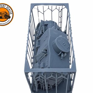 May include: A gray 3D printed model of a tank inside a gray plastic crate. The tank is upside down and the top of the turret is visible.