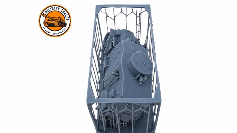 May include: A gray 3D printed model of a tank inside a gray plastic crate. The tank is upside down and the top of the turret is visible.